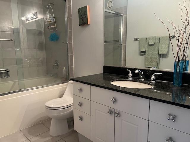 full bathroom with tile patterned flooring, combined bath / shower with glass door, toilet, and vanity