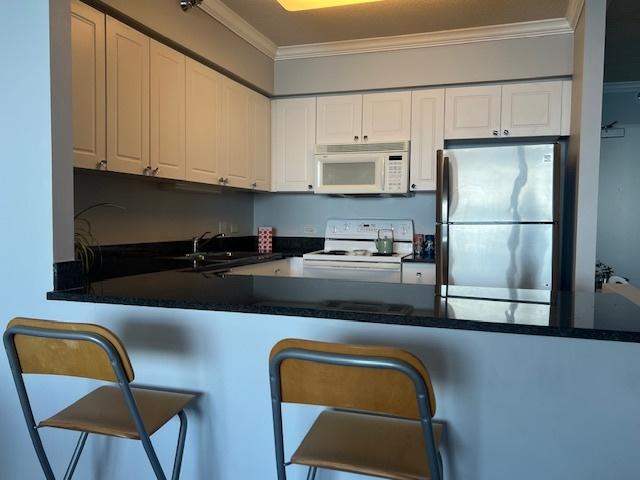 kitchen featuring white cabinetry, kitchen peninsula, crown molding, white appliances, and a breakfast bar