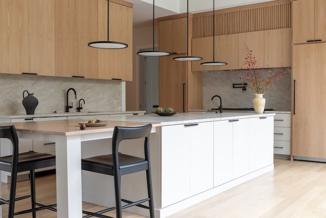 kitchen featuring pendant lighting, white cabinets, sink, light hardwood / wood-style flooring, and a kitchen bar