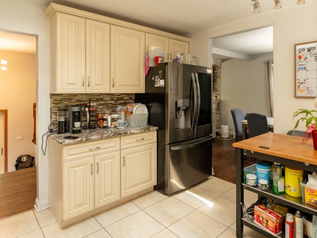 kitchen with light tile patterned flooring, decorative backsplash, light stone countertops, stainless steel fridge with ice dispenser, and cream cabinetry