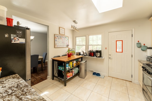 kitchen featuring appliances with stainless steel finishes, a skylight, light stone counters, light tile patterned flooring, and hanging light fixtures