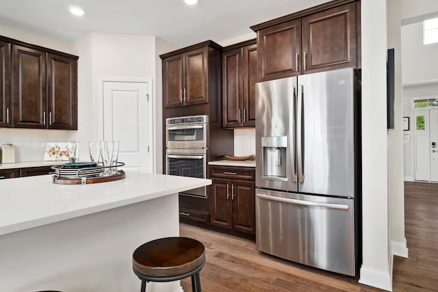 kitchen with decorative backsplash, light hardwood / wood-style flooring, dark brown cabinetry, appliances with stainless steel finishes, and a breakfast bar area