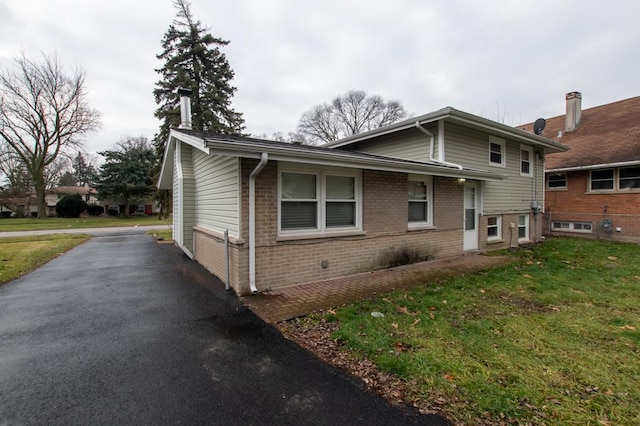 view of side of property featuring a yard, brick siding, and driveway