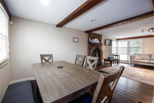 dining area with hardwood / wood-style floors, a fireplace, beamed ceiling, track lighting, and brick wall