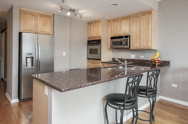 kitchen with stainless steel appliances, a breakfast bar, kitchen peninsula, and light hardwood / wood-style flooring