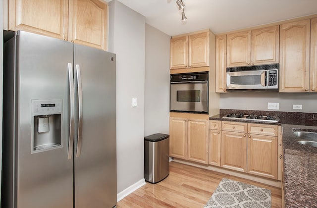 kitchen with appliances with stainless steel finishes, dark stone countertops, light wood-type flooring, and light brown cabinets