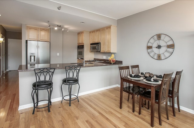 kitchen with a kitchen breakfast bar, kitchen peninsula, light brown cabinets, stainless steel appliances, and light hardwood / wood-style flooring