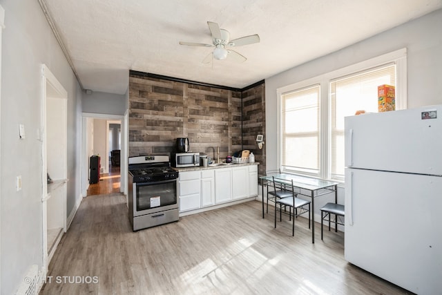 kitchen with white cabinetry, appliances with stainless steel finishes, wooden walls, ceiling fan, and light hardwood / wood-style flooring