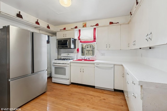 kitchen featuring light wood-style flooring, a sink, white cabinetry, light countertops, and appliances with stainless steel finishes