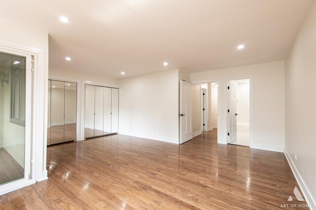 unfurnished bedroom featuring ensuite bathroom, two closets, and wood-type flooring