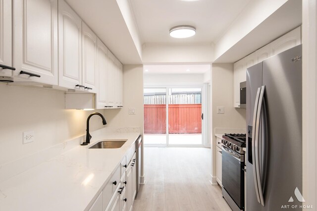 kitchen with appliances with stainless steel finishes, white cabinetry, sink, light stone counters, and light wood-type flooring