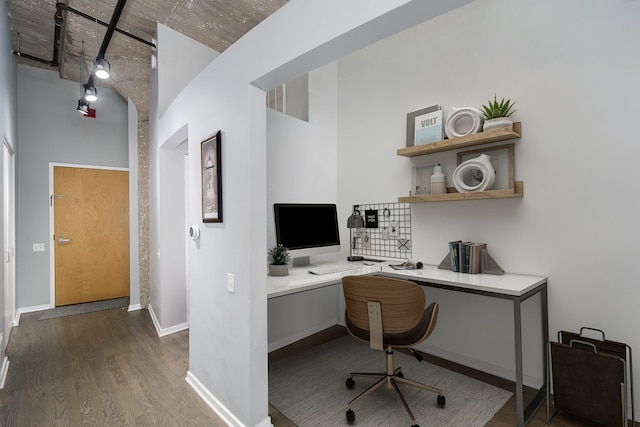 office with a towering ceiling, built in study area, baseboards, and wood finished floors