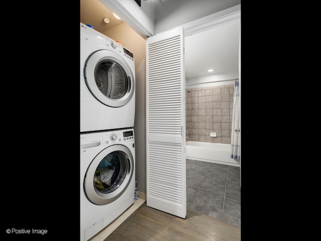 clothes washing area with stacked washer and clothes dryer, wood finished floors, and laundry area