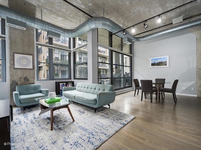 living area featuring a high ceiling, rail lighting, wood finished floors, and baseboards