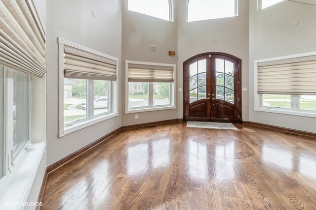 unfurnished room with a wealth of natural light, french doors, a towering ceiling, and wood-type flooring