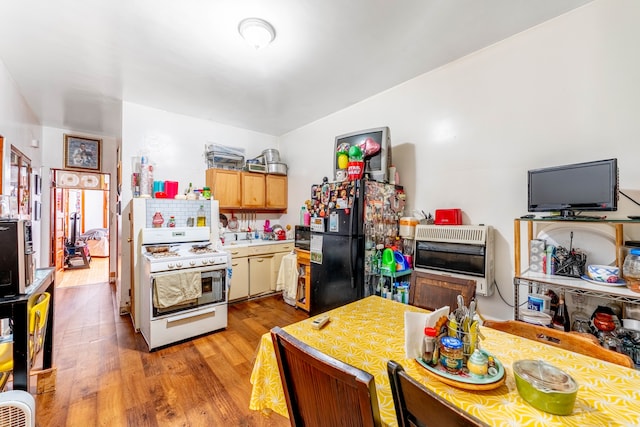 kitchen featuring black fridge, white range with gas stovetop, light brown cabinetry, and light hardwood / wood-style flooring