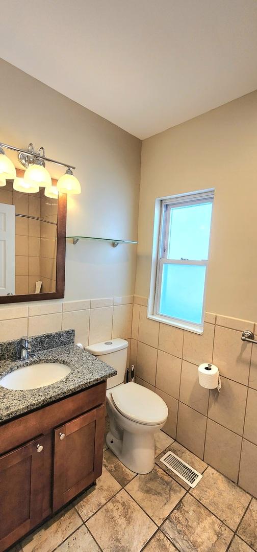 bathroom with tile walls, visible vents, toilet, wainscoting, and vanity