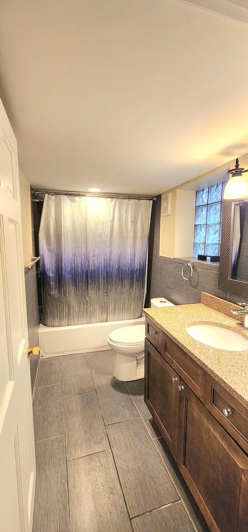 bathroom with shower / bathtub combination, toilet, vanity, and tile walls