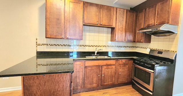 kitchen featuring stainless steel gas range oven, under cabinet range hood, a peninsula, a sink, and dark stone counters