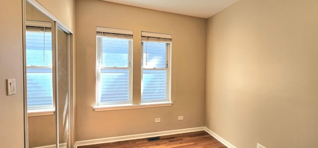 unfurnished room featuring wood finished floors, visible vents, and baseboards