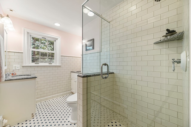 bathroom featuring vanity, toilet, tile walls, and a shower with shower door