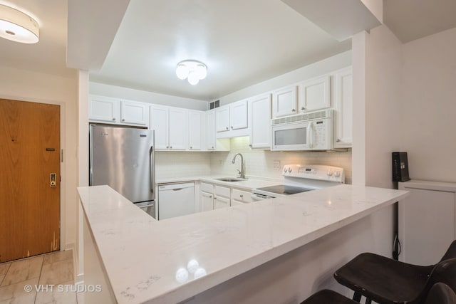 kitchen with sink, a breakfast bar, kitchen peninsula, white appliances, and white cabinets