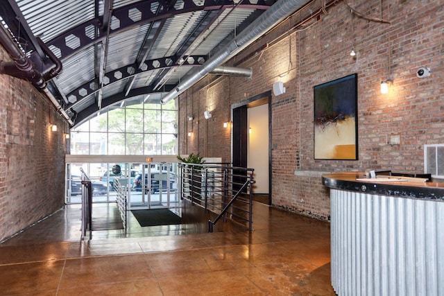 hall featuring finished concrete flooring, visible vents, a towering ceiling, an upstairs landing, and brick wall