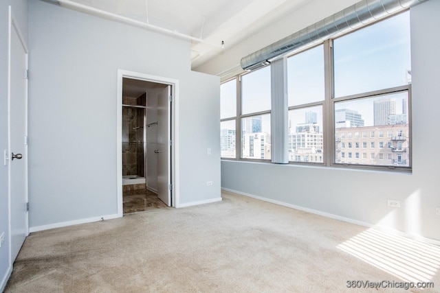 unfurnished bedroom with baseboards, carpet, ensuite bathroom, and a city view