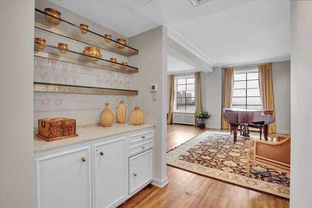 bar featuring light hardwood / wood-style flooring, radiator heating unit, and white cabinets