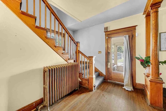 foyer entrance featuring hardwood / wood-style floors, radiator heating unit, and ornate columns