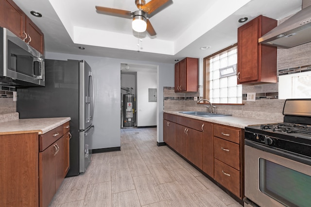 kitchen featuring a raised ceiling, backsplash, stainless steel appliances, ceiling fan, and wall chimney range hood