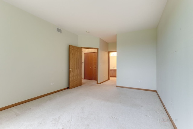 unfurnished bedroom with visible vents, baseboards, light colored carpet, and ensuite bath