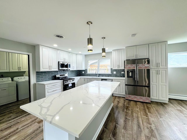 kitchen with appliances with stainless steel finishes, hardwood / wood-style flooring, independent washer and dryer, and white cabinets