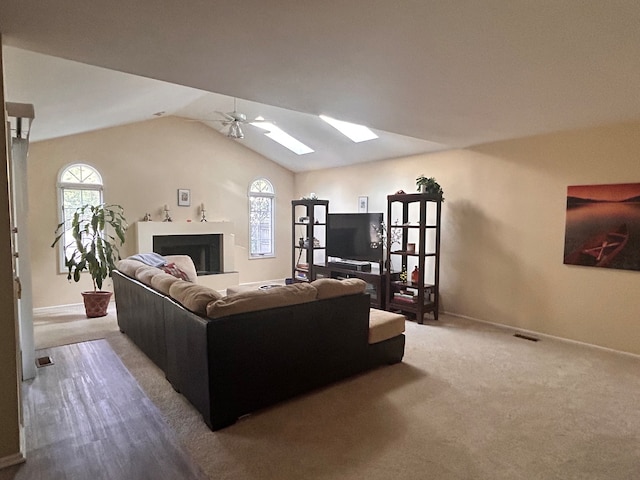 carpeted living room with vaulted ceiling with skylight and ceiling fan