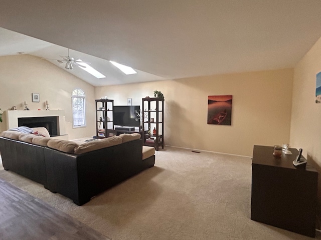 carpeted living room with ceiling fan and lofted ceiling with skylight