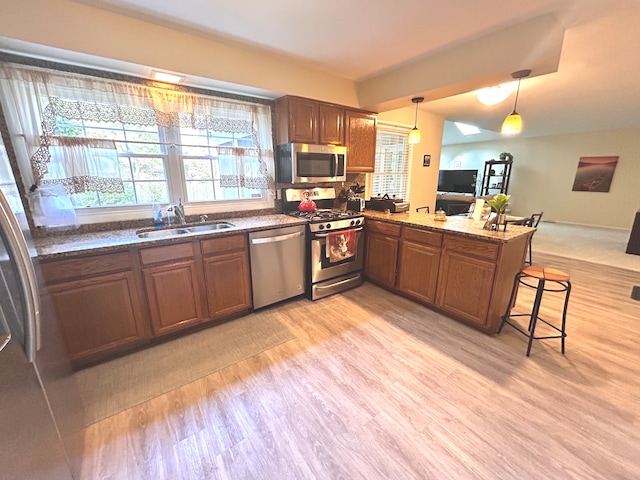 kitchen featuring appliances with stainless steel finishes, light hardwood / wood-style floors, kitchen peninsula, decorative light fixtures, and sink