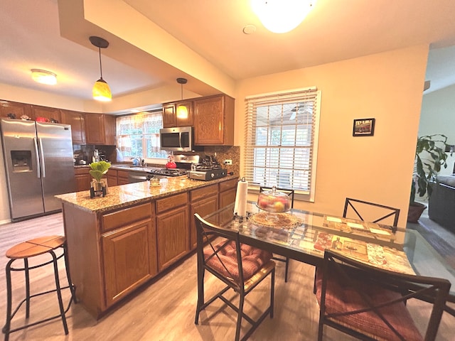 kitchen featuring pendant lighting, stone counters, stainless steel appliances, light hardwood / wood-style floors, and decorative backsplash