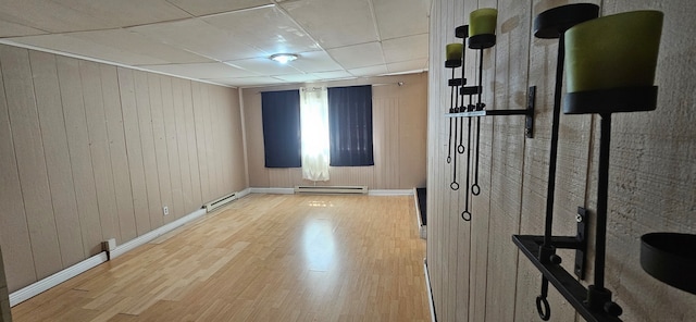 spare room featuring wood walls, a paneled ceiling, a baseboard heating unit, and light wood-type flooring