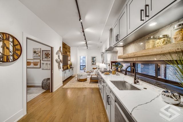 kitchen with dishwasher, sink, rail lighting, light stone counters, and light wood-type flooring