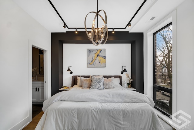 bedroom featuring rail lighting, a chandelier, dark hardwood / wood-style flooring, and ensuite bath