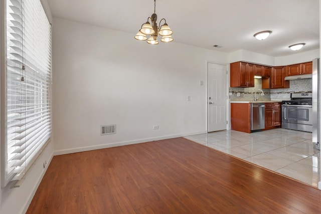 1781 Queensbury Cir, Hoffman Estates, IL 60169 - kitchen with stainless steel appliances, light countertops, under cabinet range hood, a chandelier, and light wood-style flooring