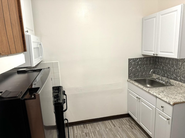 kitchen with light wood finished floors, light countertops, decorative backsplash, white cabinets, and a sink