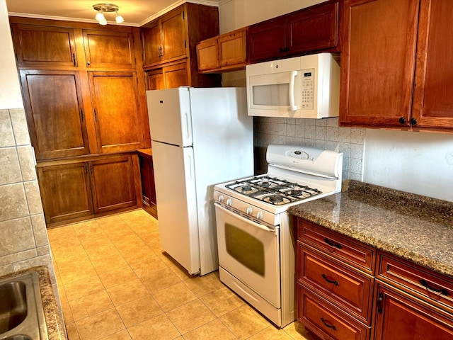 kitchen with tasteful backsplash, light tile patterned flooring, a sink, dark stone counters, and white appliances