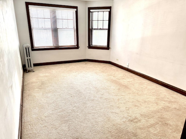 unfurnished room featuring light carpet, baseboards, and radiator