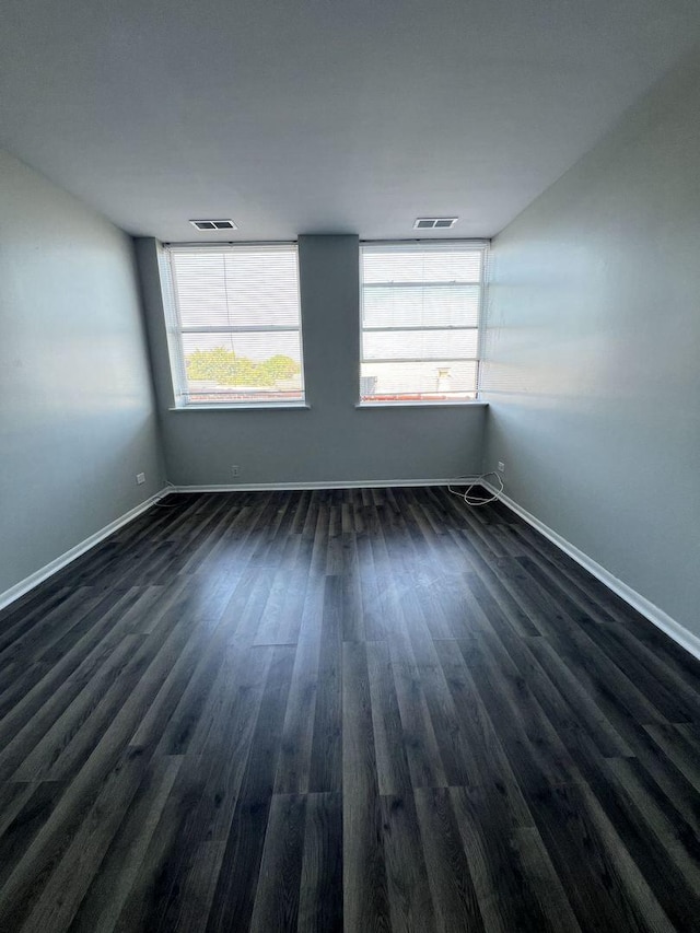 spare room with dark wood-type flooring, visible vents, and baseboards