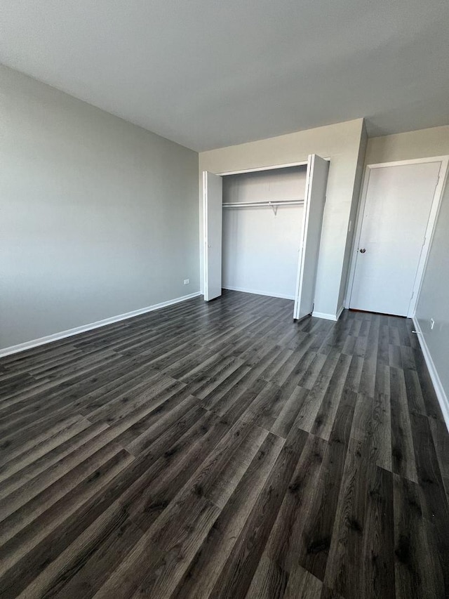 unfurnished bedroom with a closet, baseboards, and dark wood-type flooring