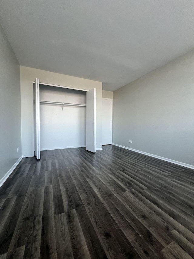 unfurnished bedroom with a closet, dark wood-style flooring, and baseboards