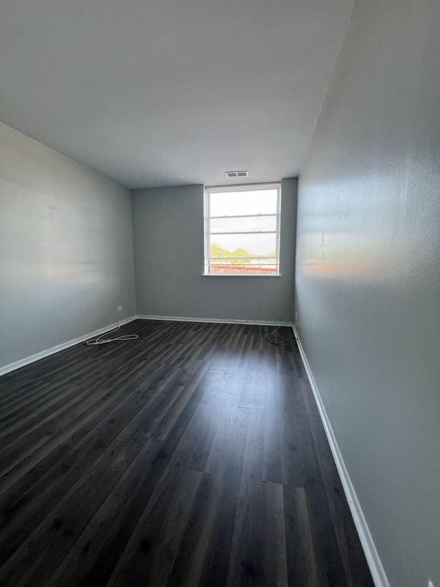 empty room featuring baseboards, visible vents, and dark wood-type flooring