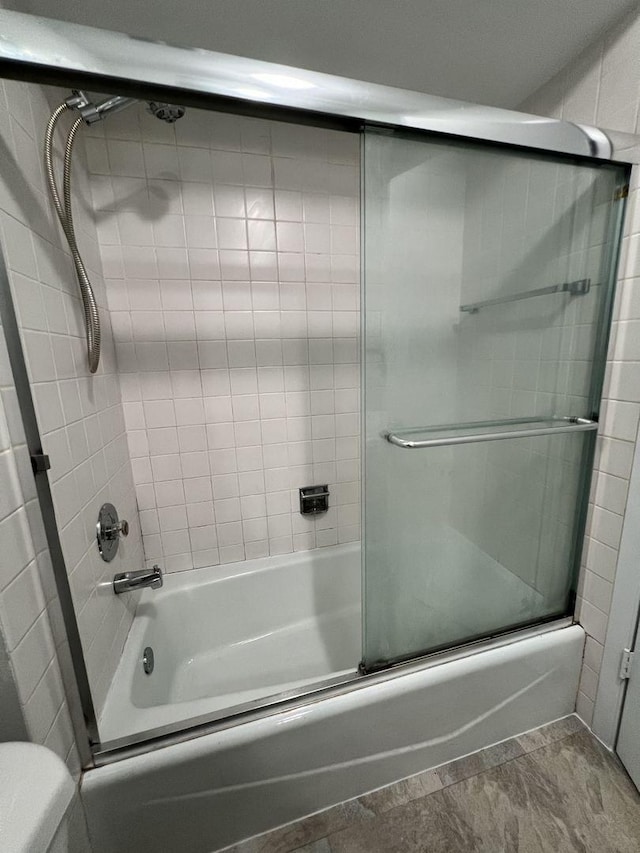 bathroom featuring combined bath / shower with glass door and toilet