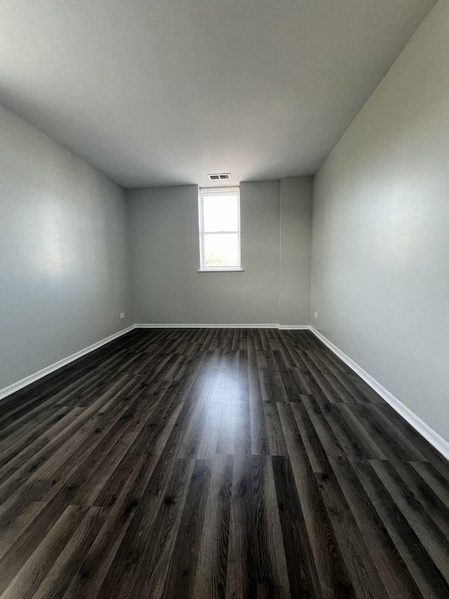 empty room with visible vents, dark wood finished floors, and baseboards